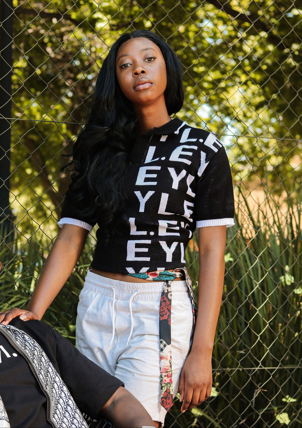 Two people standing in front of a chain-link fence with trees in the background